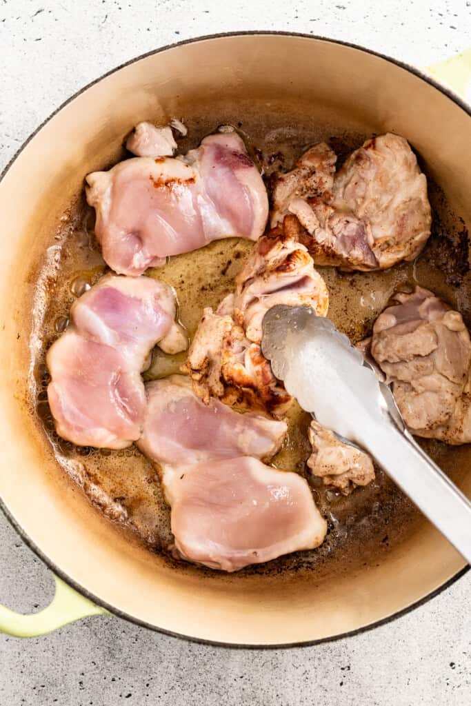 Flipping chicken thighs in a pot to brown the other side.
