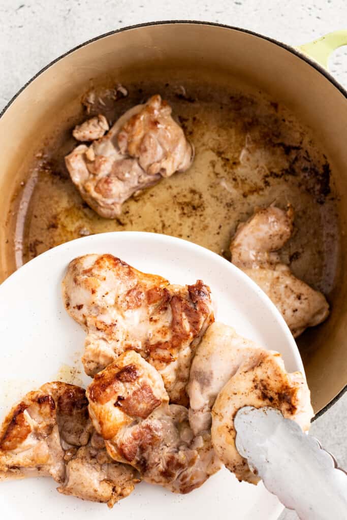 Transferring browned chicken thighs from a pot to a plate.