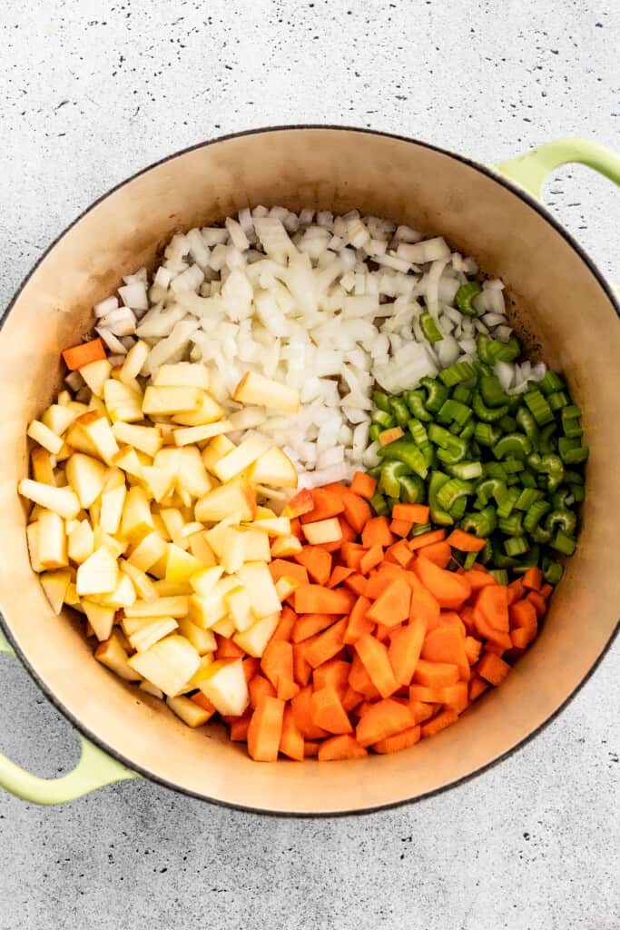 Chopped onions, celery, carrots, and potatoes in a stew pot.