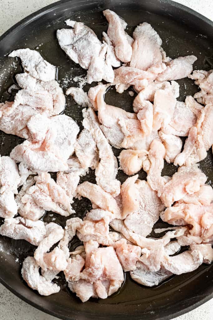Browning chicken pieces coated in cornstarch in a pan.