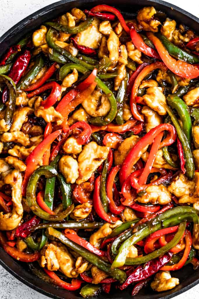 Adding sauce to chicken, sautéed bell peppers, scallions, and dried red chilis.