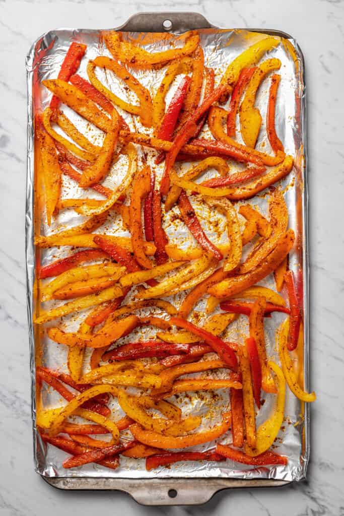 Seasoned strips of bell peppers on a sheet pan.
