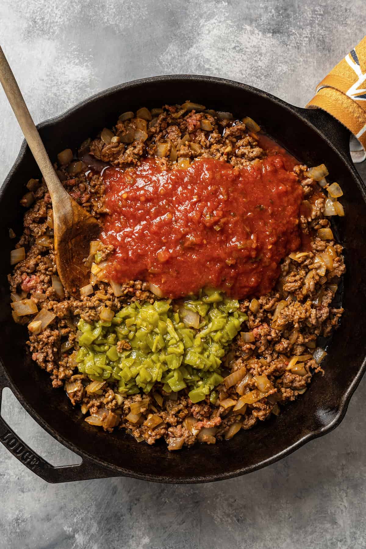 Adding salsa and canned diced green chilis to browned grownd beef in a skillet.