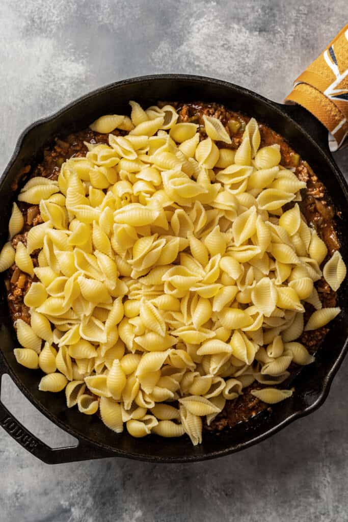 Adding cooked pasta to a skillet with sauce in it.