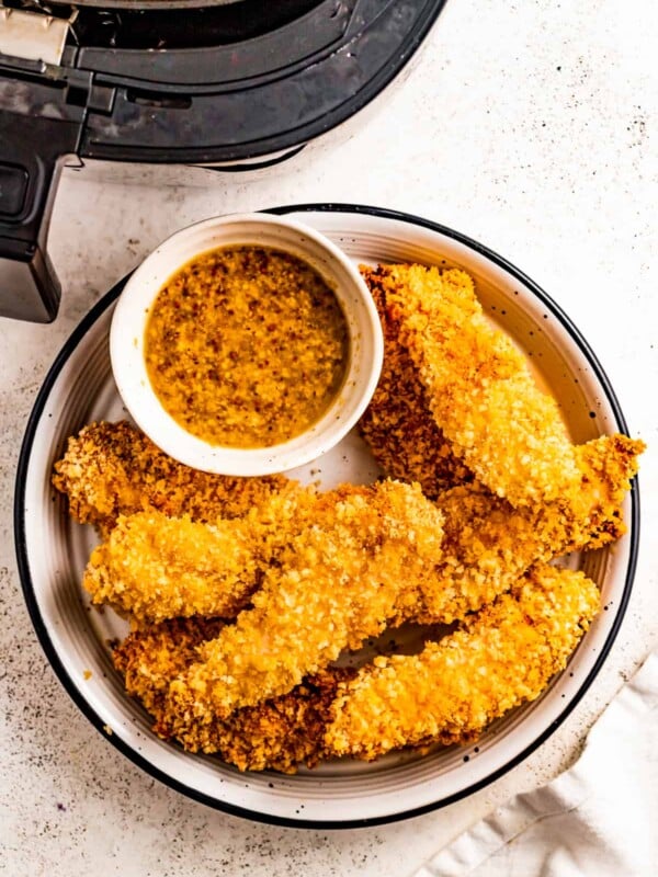 Air fryer chicken tenders on a plate with a dipping sauce on the side.