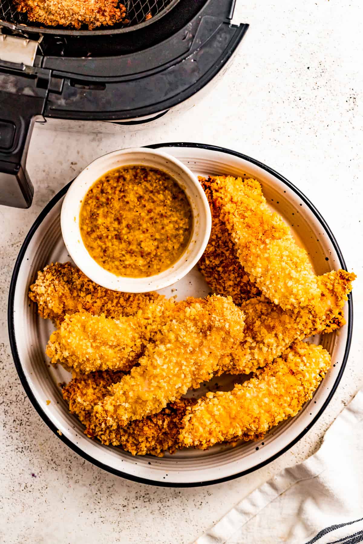 Air fryer chicken tenders on a plate with a dipping sauce on the side.
