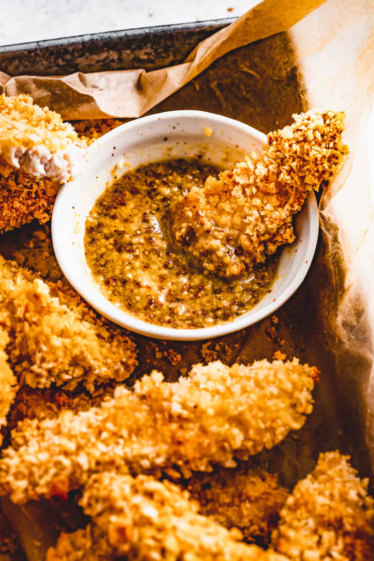 Dipping chicken tenders into a dipping sauce, with other chicken tender pieces arranged around the bowl of sauce.