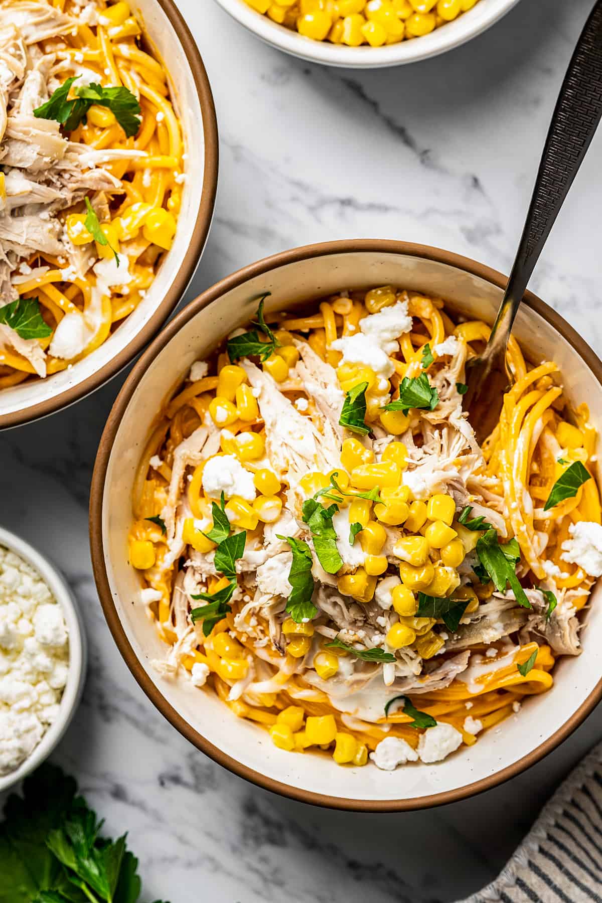 Buffalo chicken pasta in a bowl with a fork near feta and corn.