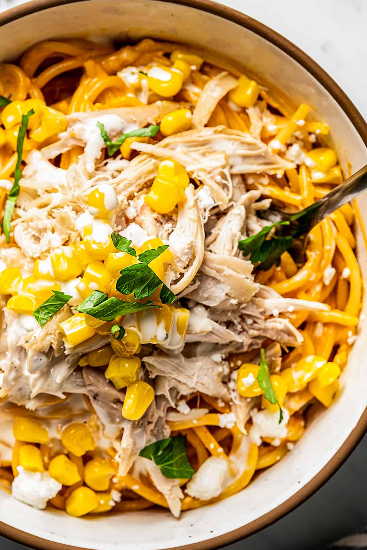 Close-up shot of Buffalo chicken pasta in a bowl with a fork near feta and corn.