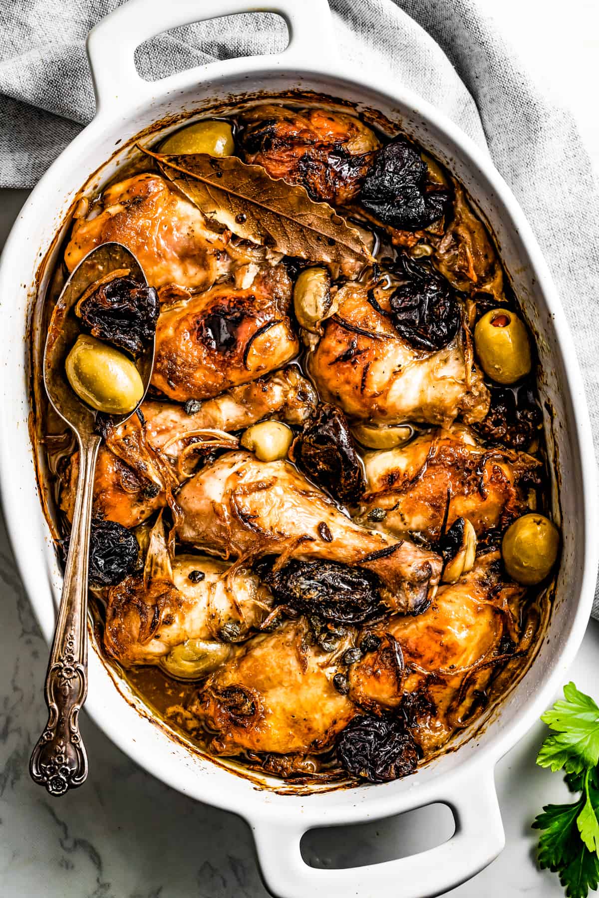 Easy chicken Marbella in a baking dish, with a gray kitchen towel placed above the baking dish.