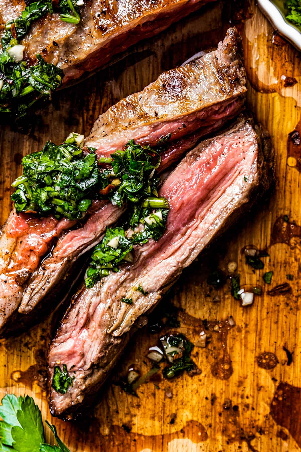 Closeup of churrasco steak on a cutting board, topped with greens.