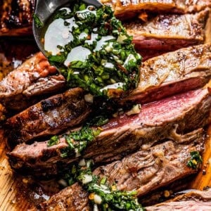 Spooning chimichurri sauce over sliced flank steak on a cutting board.
