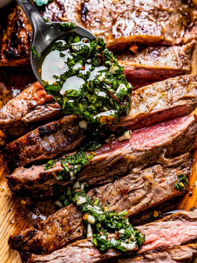 Spooning chimichurri sauce over sliced flank steak on a cutting board.