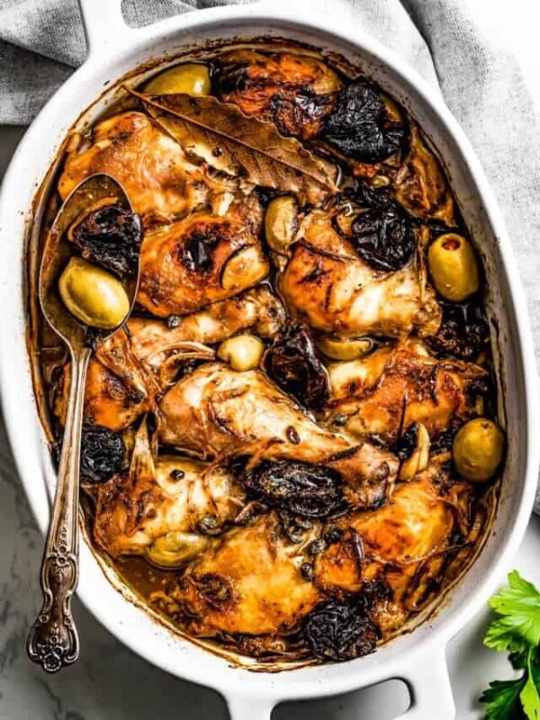 Easy chicken Marbella in a baking dish, with a gray kitchen towel placed above the baking dish.