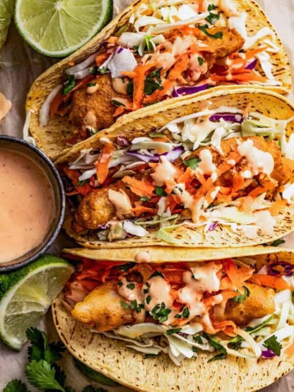 Three Mahi Mahi fish tacos on a plate with toppings and chipotle mayo on the side.