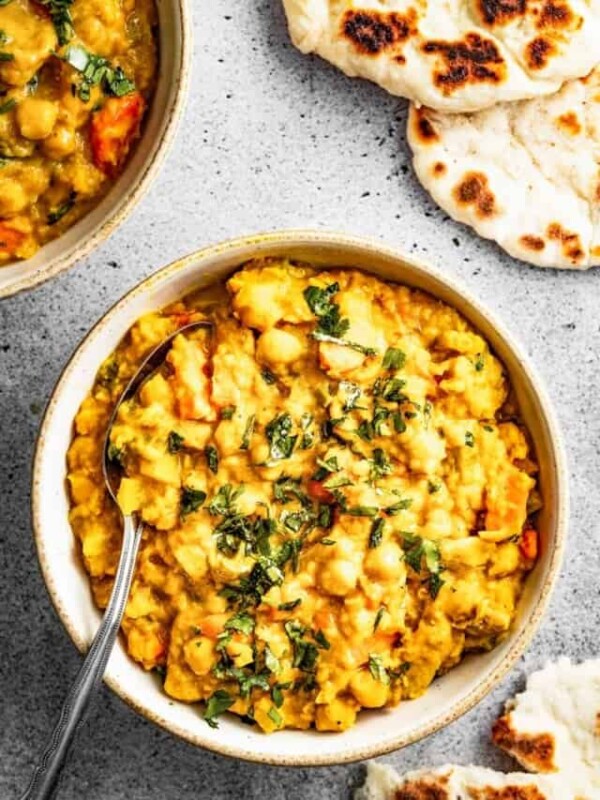 Overhead shot of Mulligatawny stew in a bowl with a spoon near a piece of naan.