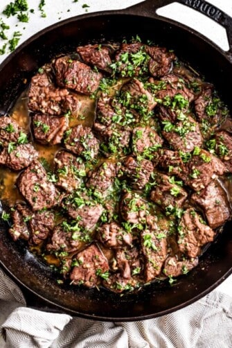 Garlic butter steak bites in a skillet, and they're topped with parsley.