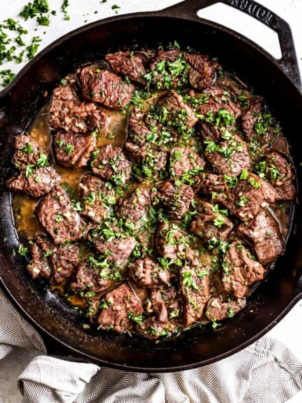 Garlic butter steak bites in a skillet, and they're topped with parsley.