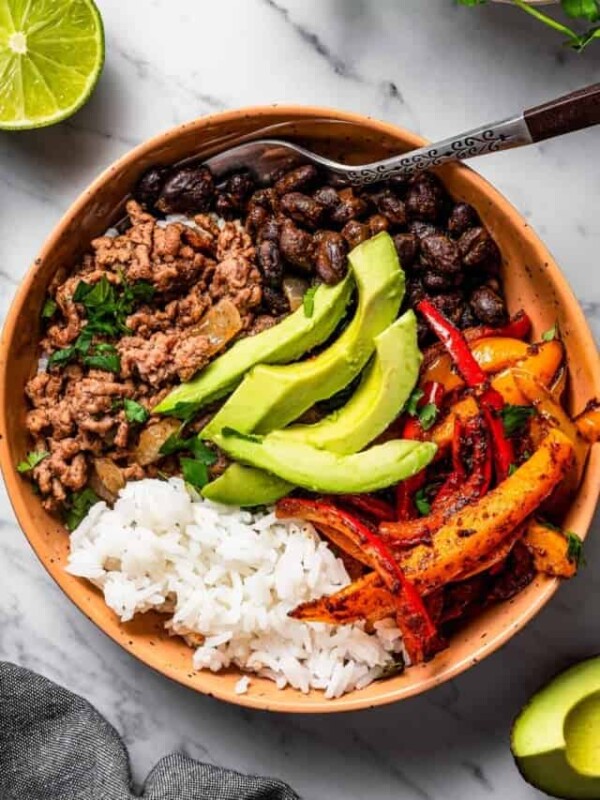 overhead shot of a taco bowl with taco meat, sliced bell peppers, avocado slices, beans, and rice, and a fork placed inside the bowl.