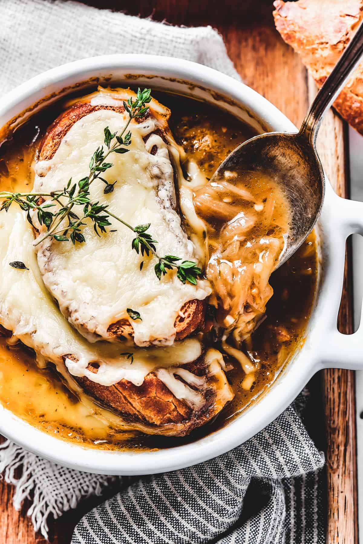 French Onion Soup served in a white bowl, with a spoon stirring through the soup.