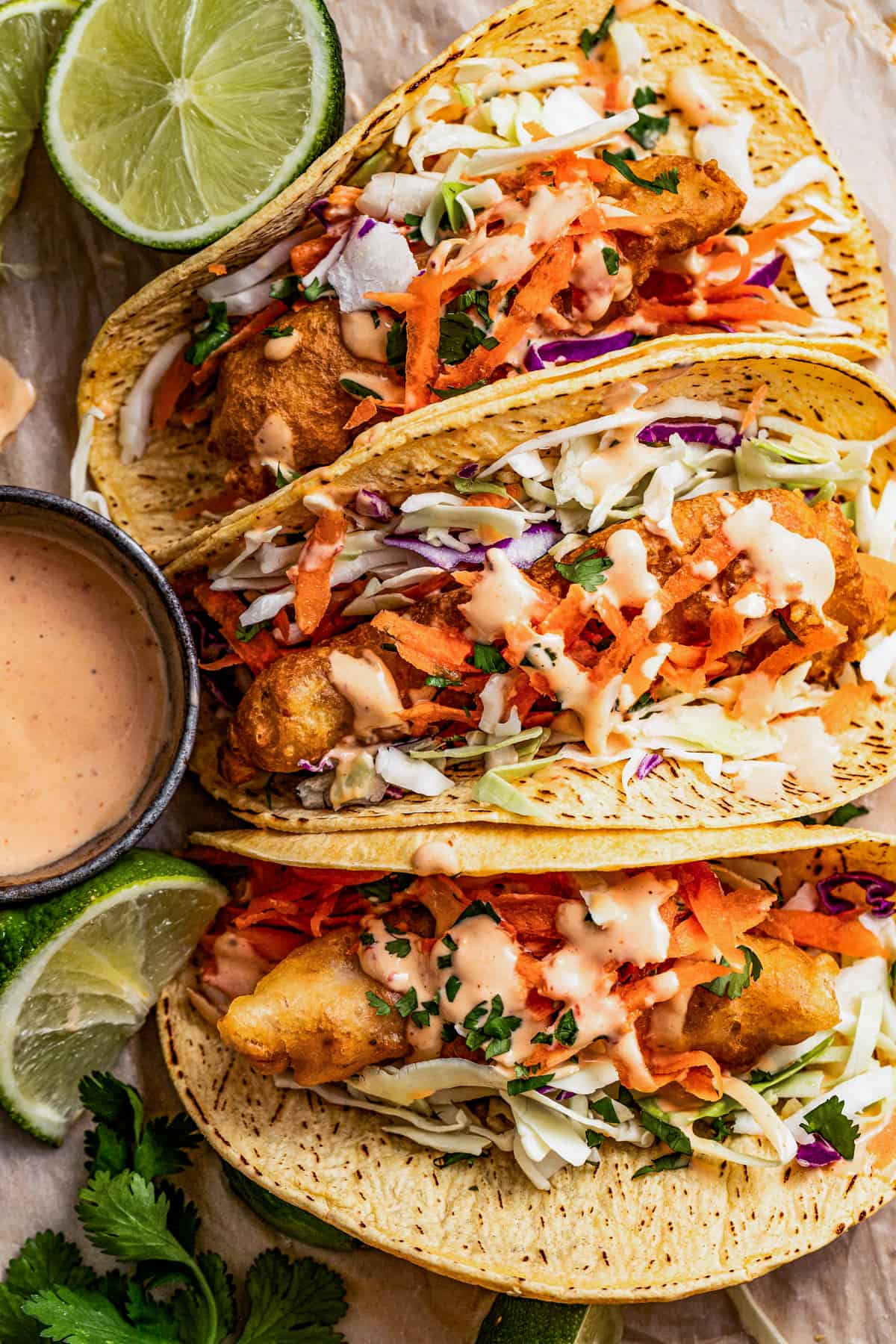 Three Mahi Mahi fish tacos on a plate with toppings and chipotle mayo on the side.