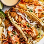 Mahi mahi fish tacos on a plate with toppings and chipotle mayo on the side.