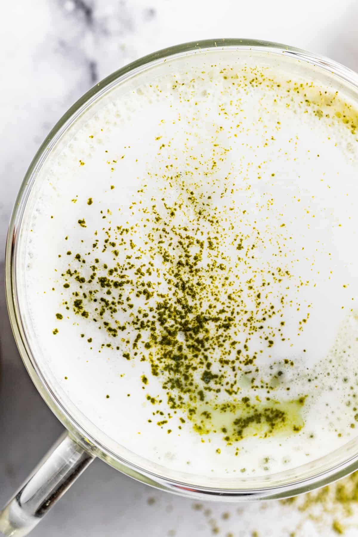 Overhead of milk foam in a matcha latte with a sprinkle of matcha powder.