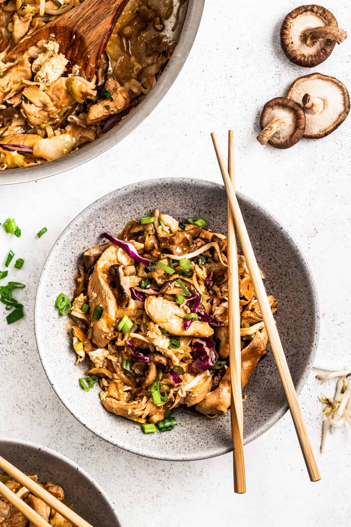Moo shu chicken in a bowl with chopsticks near a pan of moo shu chicken.