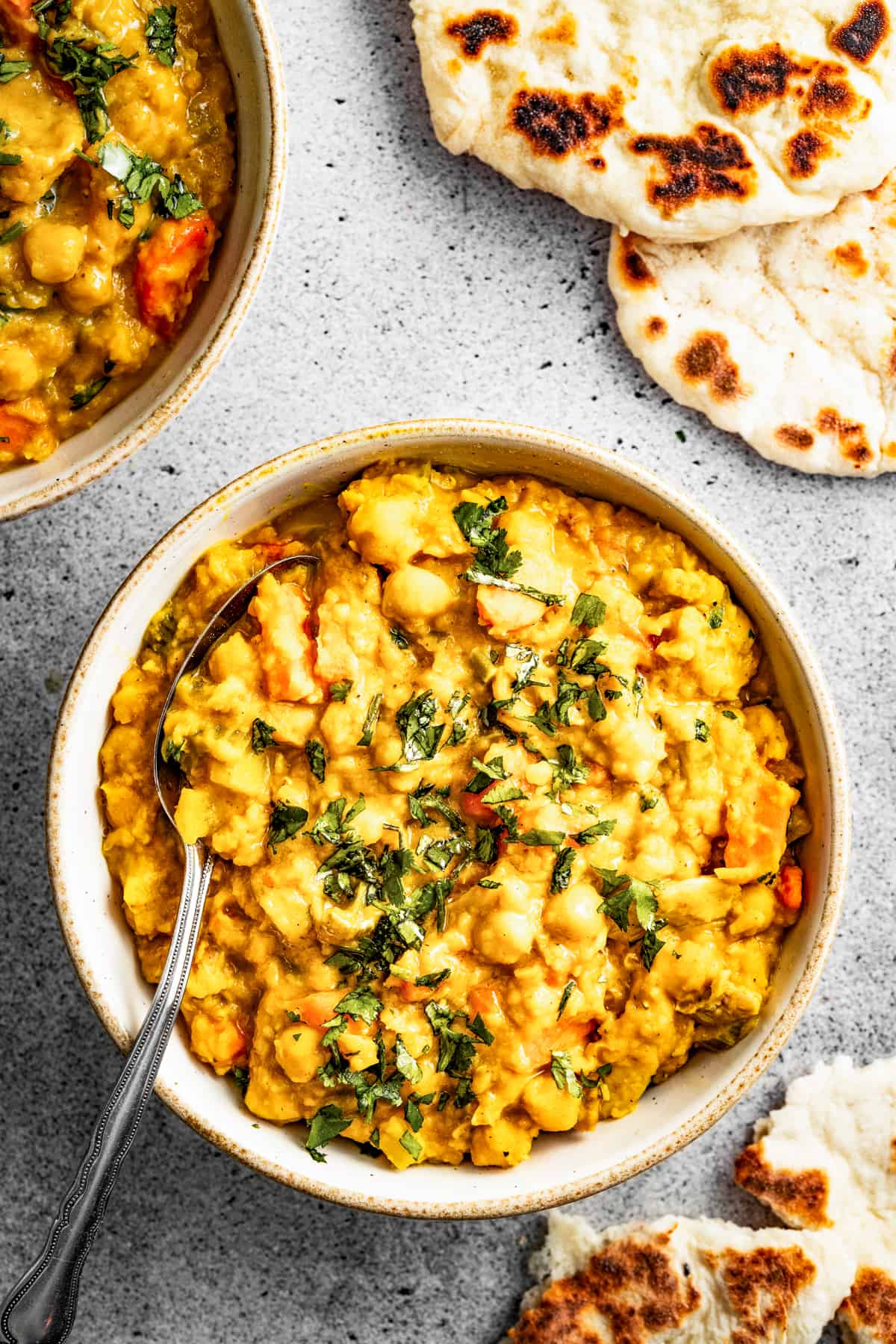 Overhead shot of Mulligatawny stew in a bowl with a spoon near a piece of naan.