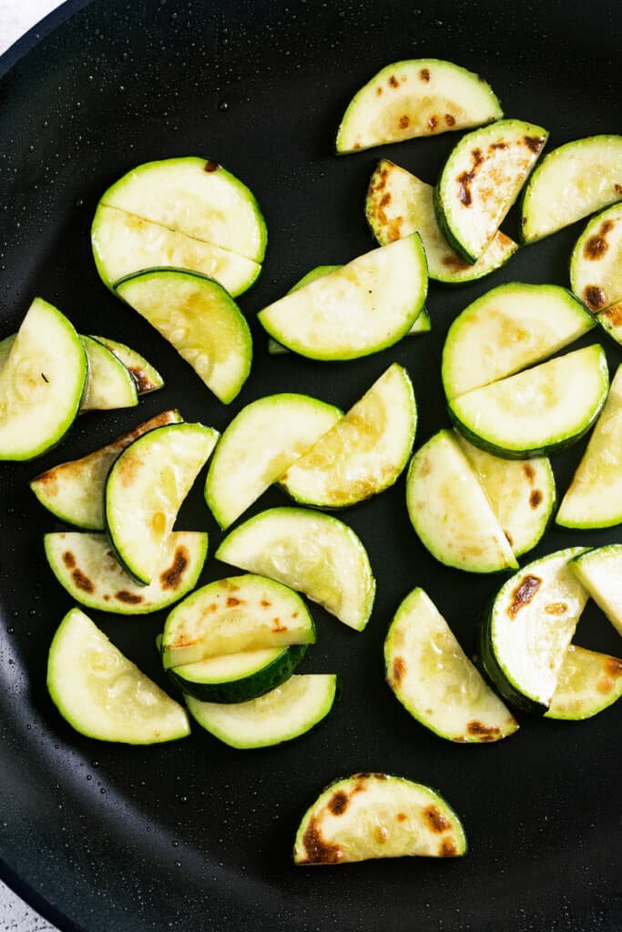Cooking sliced zucchini in a black skillet.