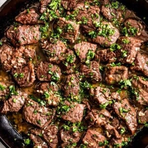 Garlic butter steak bites in a cast iron skillet, and they're garnished with parsley.
