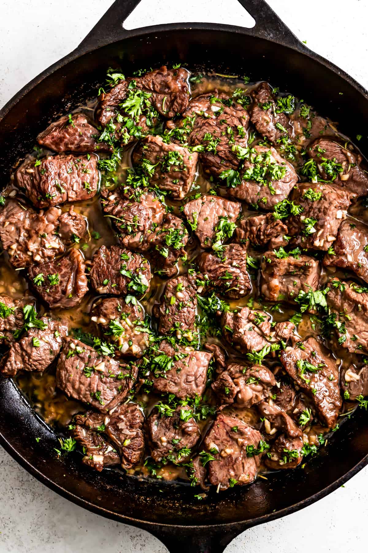 Garlic butter steak bites in a cast iron skillet, and they're garnished with parsley.