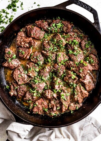 Garlic butter steak bites in a skillet, and they're topped with parsley.