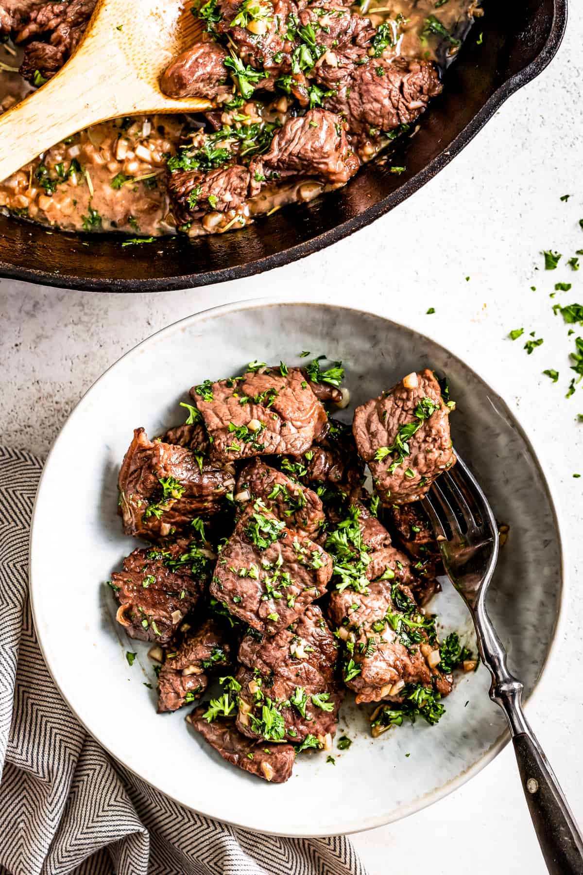 Transferring the garlic butter steak bites from a skillet to the plate.