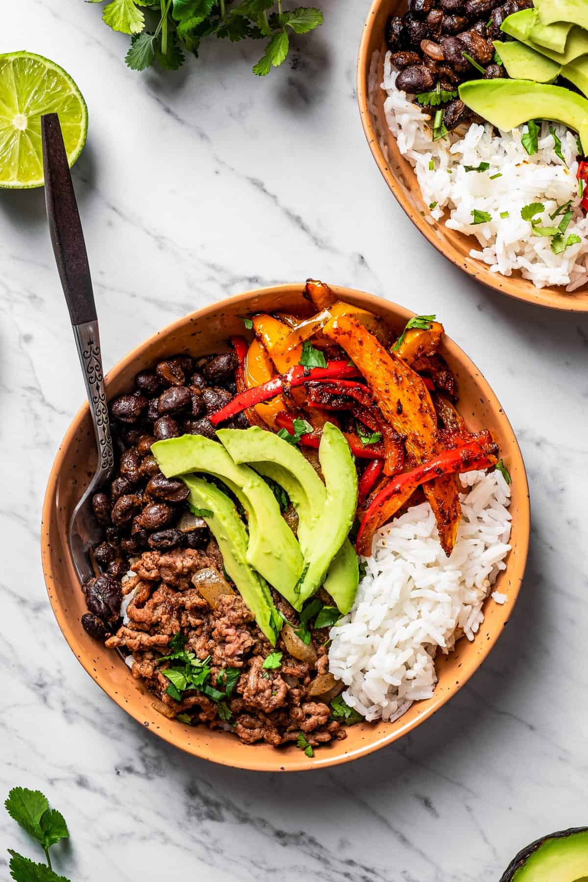 two Taco bowls on a table near fresh lime and 2 forks.