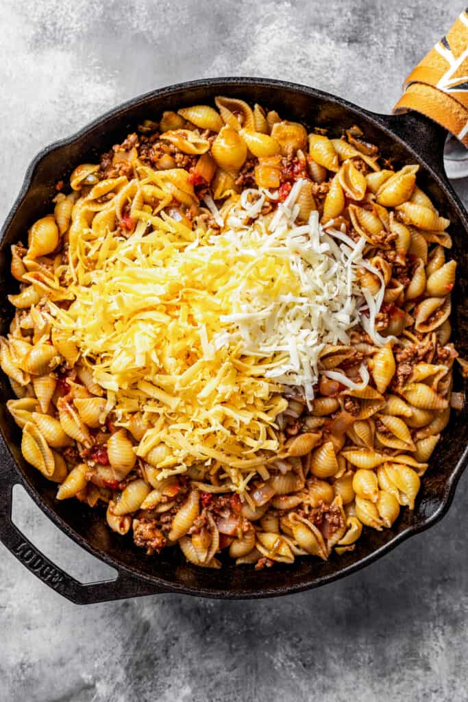 Adding shredded cheese to pasta shells in a skillet.