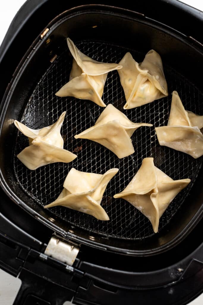 Uncooked crab rangoon in the basket of an air fryer.