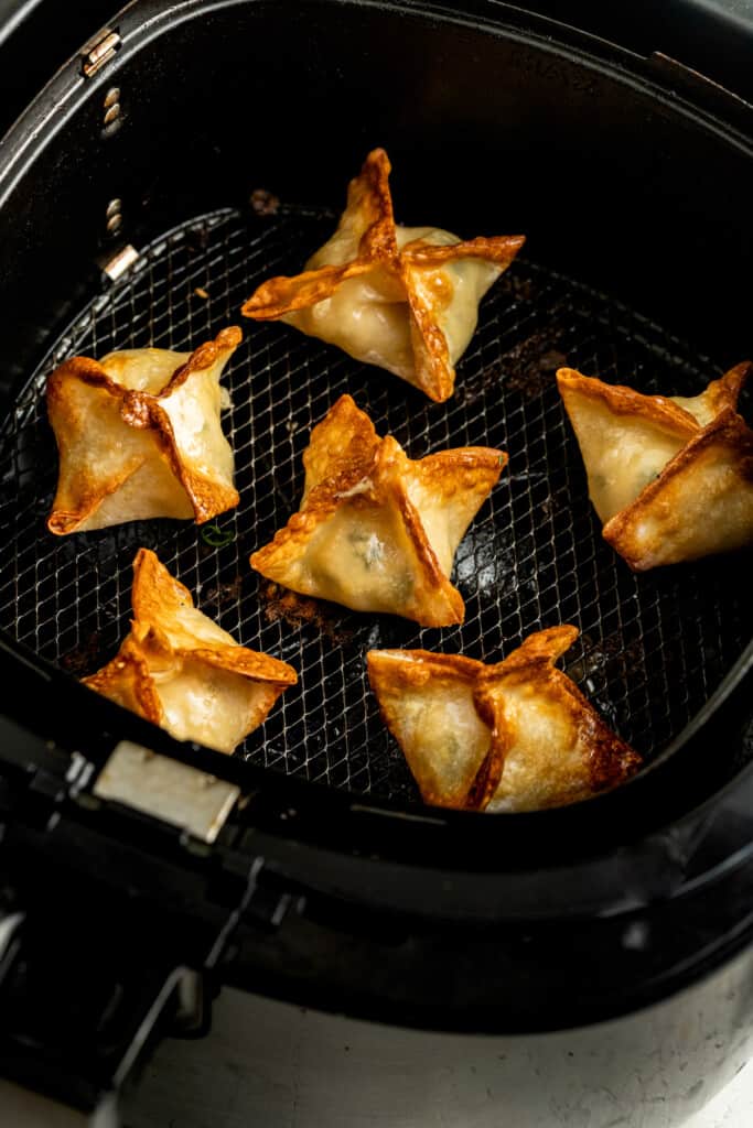 Crab rangoon cooked in the basket of an air fryer.