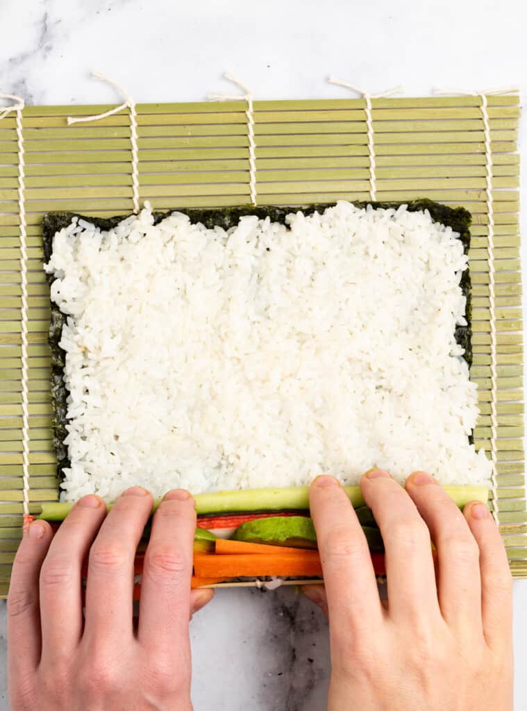 Beginning to roll rice and nori around a filling to make maki.