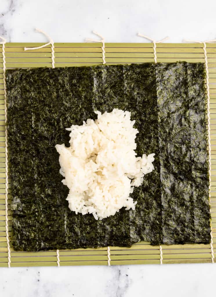 Adding rice to sushi nori on a sushi mat.