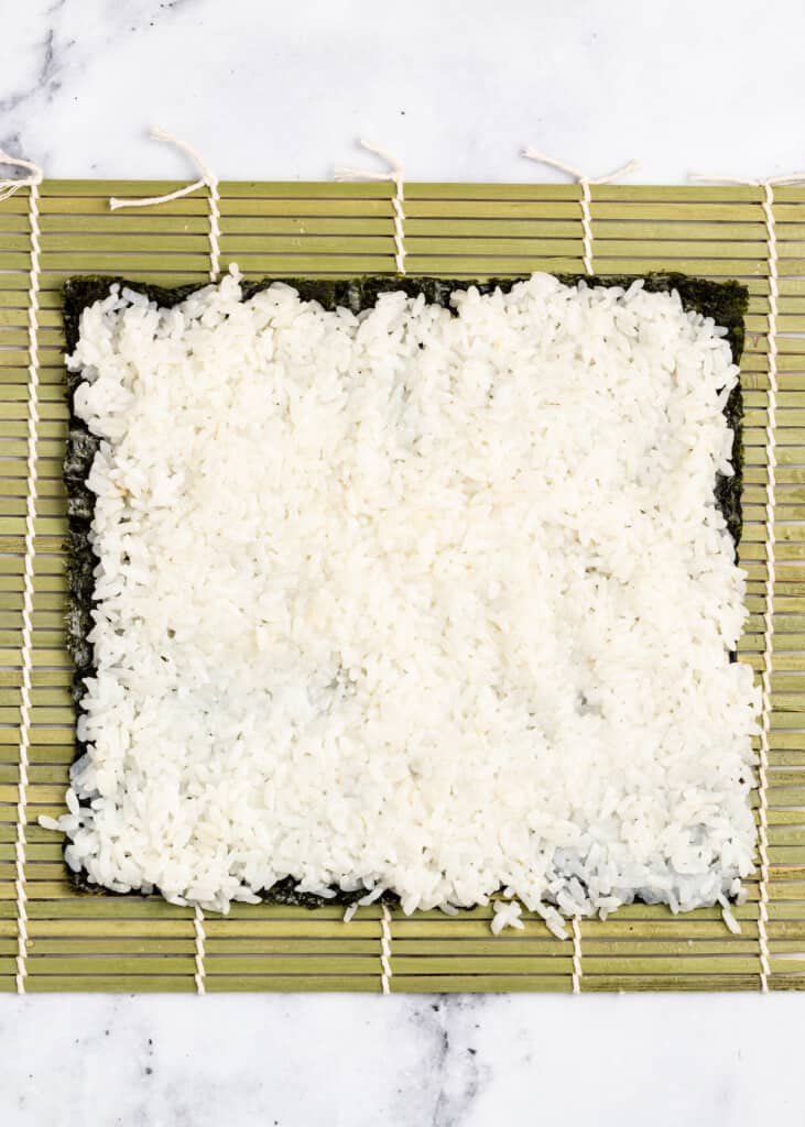 Sushi rice spread over nori on a sushi mat.