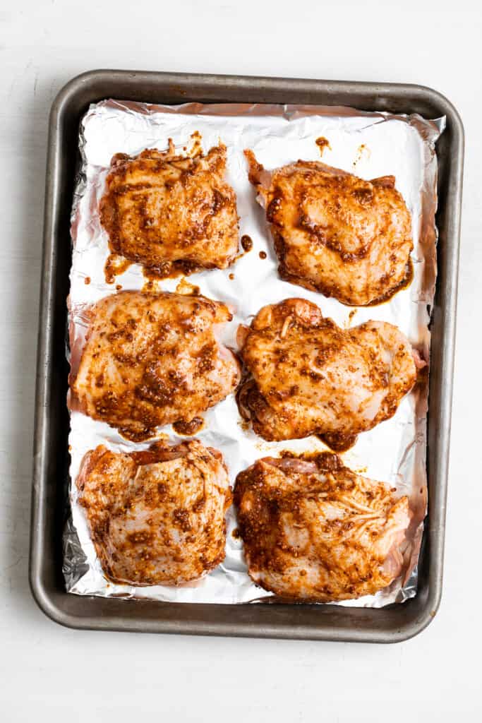 Chicken thighs coated in olive oil, lime, and spices on a baking sheet lined with aluminum foil.