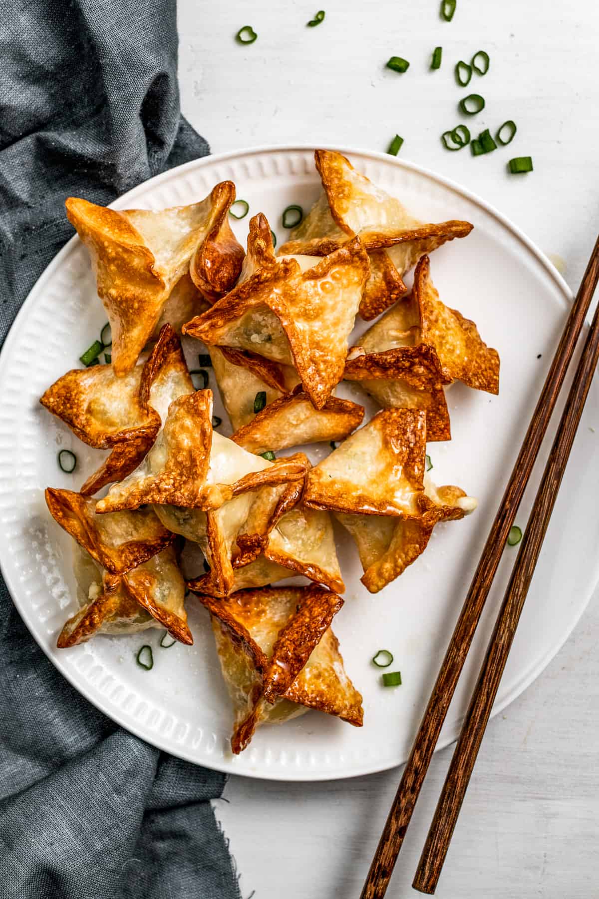 Crab rangoon on a white plate garnished with green onions and a pair of chopsticks placed next to the rangoons.