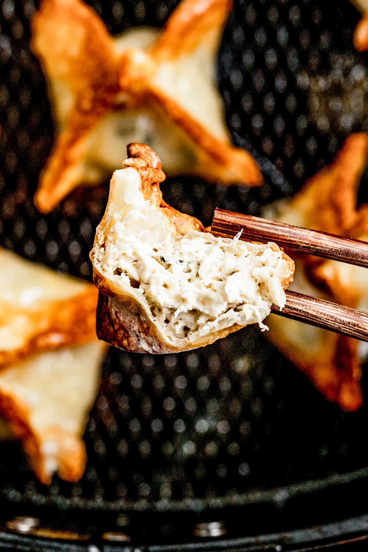 Using chopsticks to pick up a piece of crab rangoon with a bite taken out of it above an air fryer.