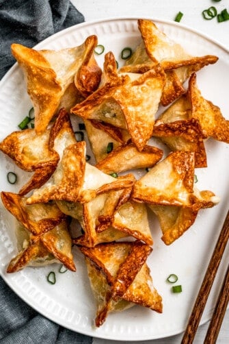 Air Fryer Crab rangoon on a white plate garnished with green onions and a pair of chopsticks placed next to the rangoons.