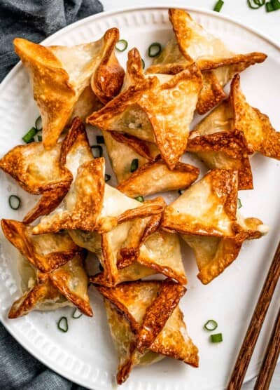 Air Fryer Crab rangoon on a white plate garnished with green onions and a pair of chopsticks placed next to the rangoons.