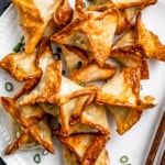 Air Fryer Crab rangoon on a white plate garnished with green onions and a pair of chopsticks placed next to the rangoons.