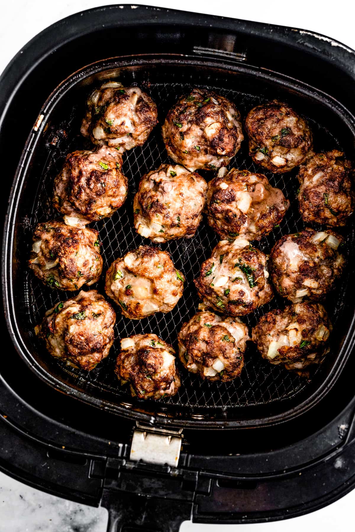Overhead shot of meatballs cooking in an air fryer basket.