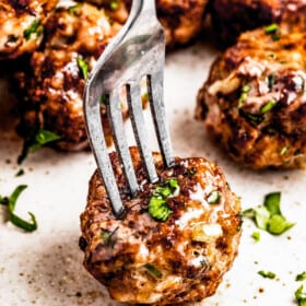 A fork piercing through an air fryer meatball served on a plate with other meatballs.