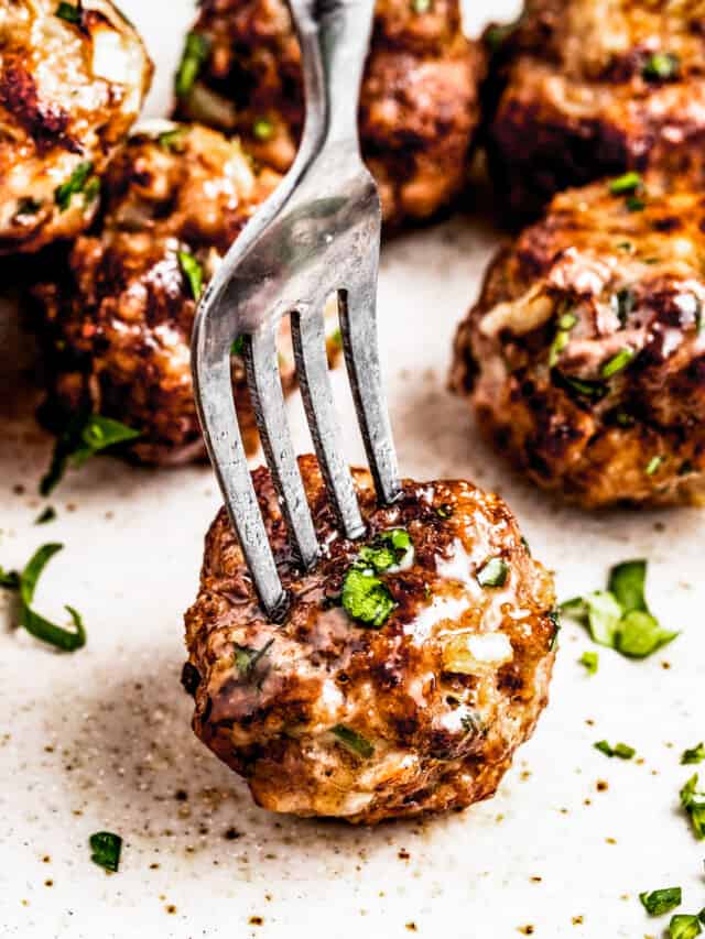 A fork piercing through an air fryer meatball served on a plate with other meatballs.